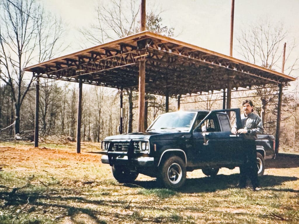 A vintage photo of John standing next to the framing of his first structure, the Greenfield Excursion stage