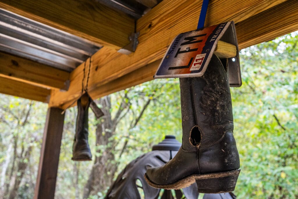 An abstract art piece featuring a hanging, modified cowboy boot with a bent South Carolina license plate above it