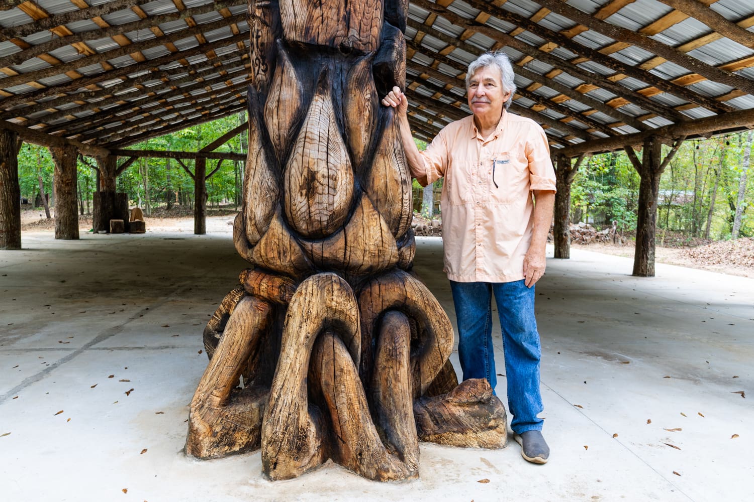 John Featherston standing next to a large carved totem that sits as part of a structure