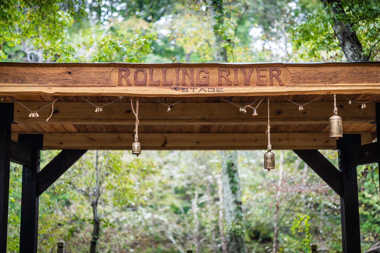 A close up of the Rolling River stage, featuring its name and a landscape scene carved and burned in to the wood