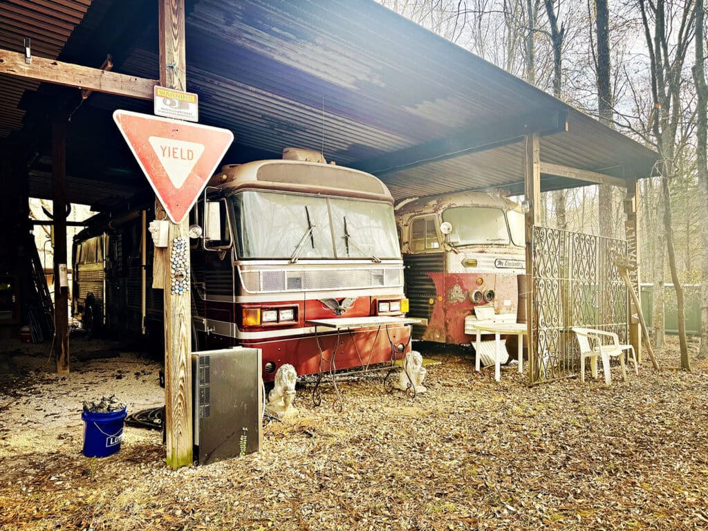 The "Bus Shed" at Stone Man Park, built from repurposed materials, with wooden beams and a metal roof. Under the cover sits 2 vintage red busses